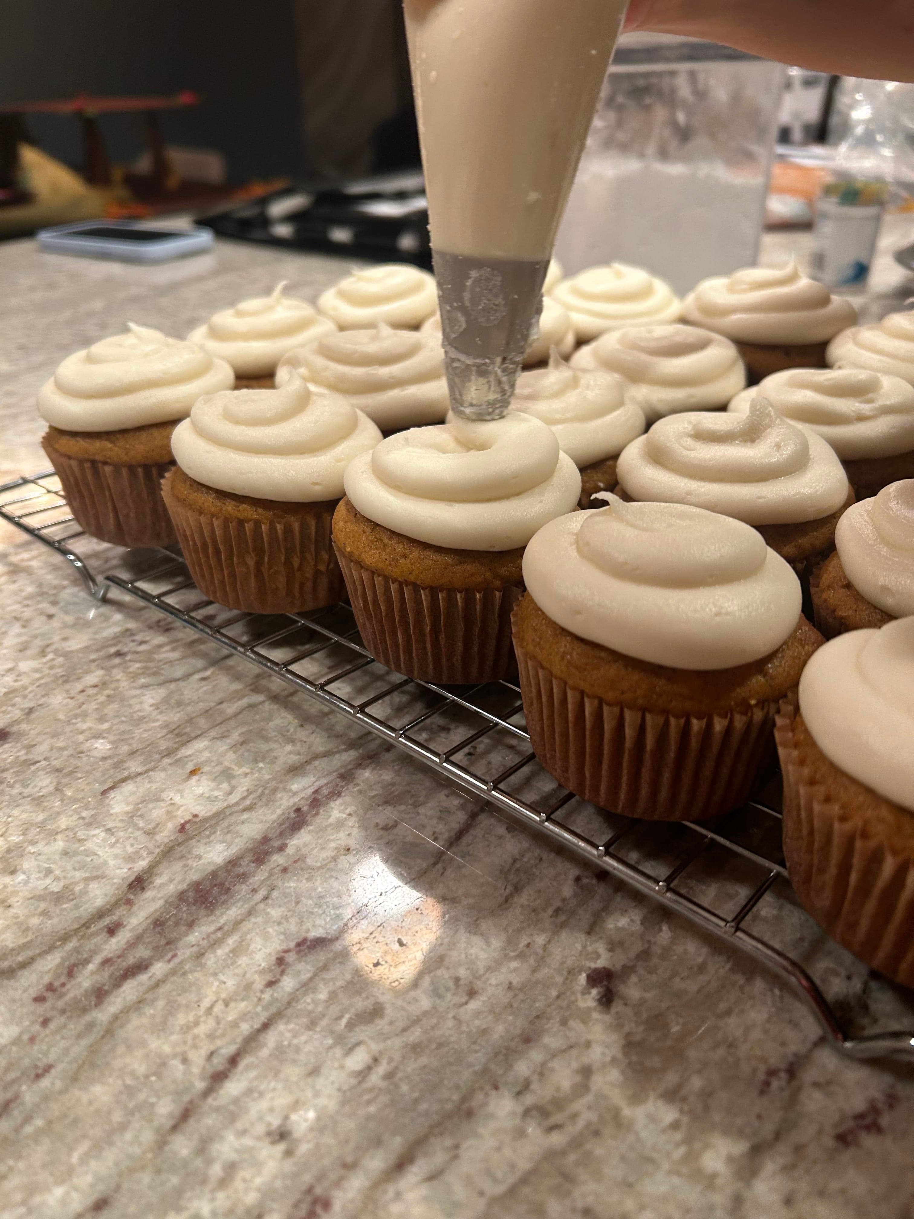 Cupcakes being piped with cream frosting